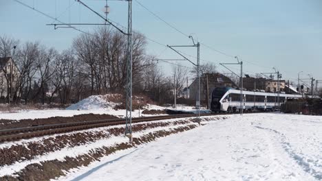 Medium-wide-shot-of-an-electric-passenger-train-entering-a-town-covered-with-snow-during-winter-in-daytime