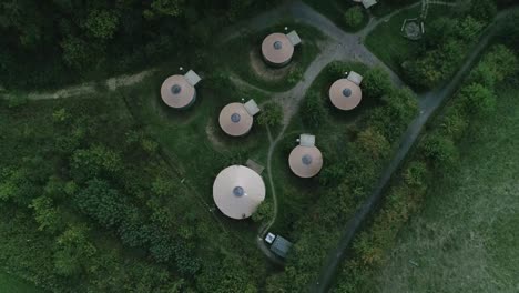Birdseye-top-down-aerial-tracking-forward-over-a-group-of-Glamping-huts-surrounded-by-forest-and-green-countryside