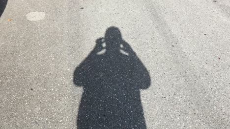 Man-Films-His-Shadow-Walking-Along-An-Asphalt-Road-With-His-Phone