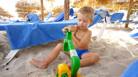 Baby-boy-sitting-on-the-sand-plays-alone-with-a-plastic-scraper,-during-the-day