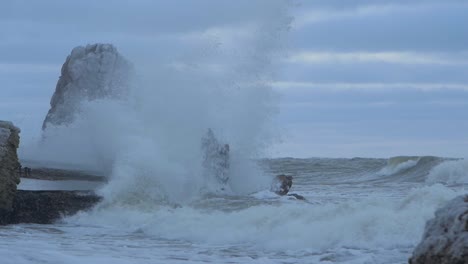 Big-stormy-waves-breaking-against-abandoned-seaside-fortification-building-ruins-at-Karosta-Northern-Forts-in-Liepaja,-slow-motion-medium-shot