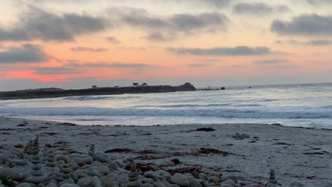 Wunderschöner-Sonnenuntergang-Am-Kiesstrand,-Kalifornien,-Mit-Surfern,-Die-Im-Hintergrund-Wellen-Reiten