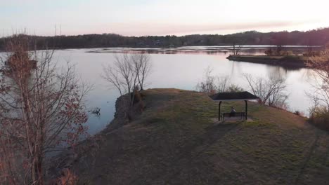 Drone-footage-flying-over-a-point-of-land-over-the-lake-with-a-swing-and-someone-sitting-in-it-below-at-sunset