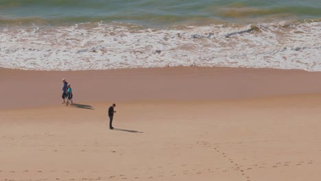 Man-ignoring-the-world-around-him,-using-his-phone-on-a-beach