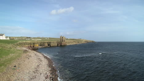 Aerial-rising-shot-moving-across-the-coastline-towards-Keiss-Castle-on-a-sunny-day,-Caithness,-Scotland