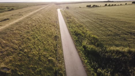 drone-is-heading-down-the-dyke-road-into-the-sun,-scenic-landscape,-sunset
