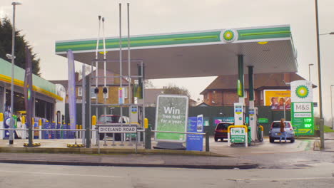 ZOOM-OUT-Gas-filling-station-with-convenience-store-in-a-London-suburb-with-female-customer-running-to-her-car