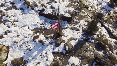 Aerial-drone-orbit-shot-of-an-American-flag-hanging-on-a-snowy,-rocky-mountain-top