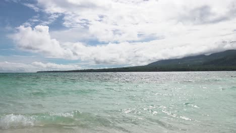 Nahaufnahme-Von-Wellen-Mit-Palmenbedeckter-Paradiesinsel-Im-Pazifischen-Ozean-Mit-Weißen,-Flauschigen-Wolken-Und-Blauem-Himmel