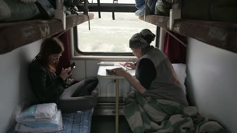 Two-women-sitting-face-to-face-in-a-small-passenger-cabin-on-a-train-running-through-Kazakhstan
