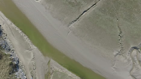 Aerial-top-down-view-of-the-a-river-in-the-sandy-bay-at-low-tide,-on-a-bright-and-sunny-day