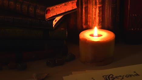 Close-up-background-of-an-ancient-library,-next-to-a-frieplace,-with-old-books,-old-paper,-stones,-and-a-candle-with-flickering-flame