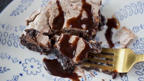 Eine-Gabel-Beißt-Aus-Einer-Gebackenen-Brownie-Dessertscheibe,-Garniert-Mit-Baiser-Und-Beträufeltem-Schokoladensirup