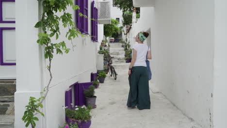 Una-Mujer-Caminando-Por-Una-Estrecha-Calle-Encalada-Con-Ventanas-De-Color-Púrpura