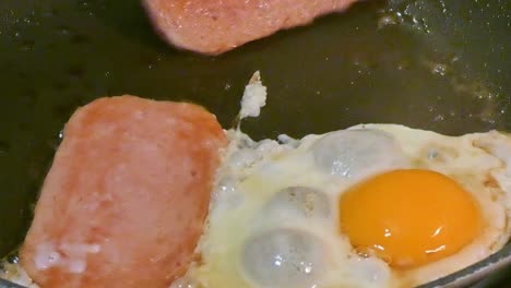 Spam-and-egg-sizzling-in-a-frying-pan-eggs-sunny-side-up-High-cholesterol-breakfast