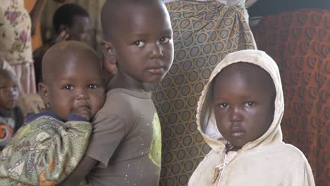 Close-up-shot-of-young-African-siblings-faces-as-a-young-baby-holds-onto-the-back-of-a-young-child-in-a-community-center