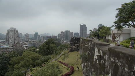 View-of-side-wall-of-Fortaleza-do-Monte-and-Macau-cityscape-with-old-buildings-on-a-gray-cloudy-overcast-day,-Macau,-Macau-SAR,-China