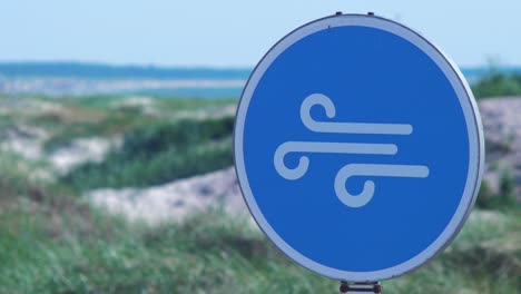 Blue-high-wind-sign-at-Liepaja-beach-dunes-in-hot-sunny-day,-close-up-shot