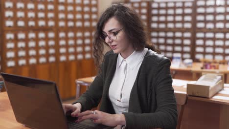 Smiling-female-student-types-on-her-laptop-at-a-wooden-desk-in-the-library