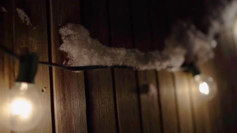 Outdoor-Patio-Lights-hanging-on-a-Fence,-covered-in-snow,-slow-motion-pan