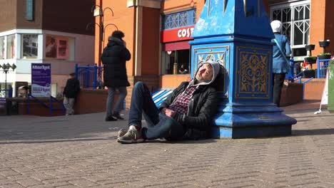 A-homeless-man-asleep-in-the-city-centre-people-just-walking-by-outside-the-biggest-shopping-centre-in-the-city,-Intu-Potteries