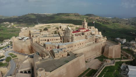 Forward-drone-aerial-shot-of-Citadella-a-historical-medieval-fortress-found-on-the-beautiful-island-of-Gozo,-Malta-in-4K-quality-with-green-hills-surrounding-it