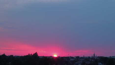 Zeitraffer-Eines-Wunderschönen-Malerischen-Roten-Sonnenuntergangs-über-Der-Stadt,-Wobei-Die-Sonne-Durch-Die-Wolken-Scheint,-Weitwinkelaufnahme