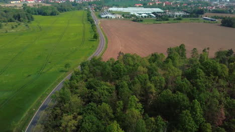 Aerial-view-of-cars-driving-on-a-road-betwenn-fields-and-forest-in-a-rural-area