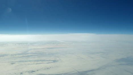 Incredible-view-from-the-cockpit-of-an-airplane-flying-high-above-the-clouds-leaving-a-long-white-condensation-vapour-air-trail-in-the-blue-sky