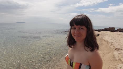 Ein-Brünettes-Mädchen-Trägt-Badebekleidung-Und-Lächelt-An-Einem-Sonnigen-Tag-An-Einem-Sandstrand-Im-Mittelmeer-In-Die-Kamera