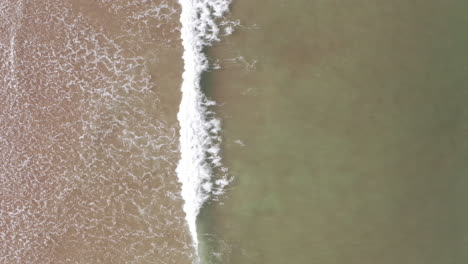 Moving-Aerial-Shot-of-Ocean-Waves-Breaking-with-a-Lone-Surfer-Paddling
