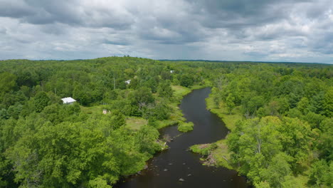 Drone-view-of-a-river-with-cottages-along-the-shore-on-a-cloudy-day