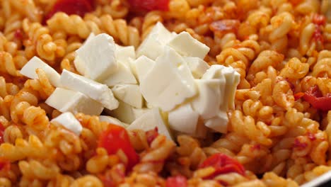 Dropping-mozarella-chunks-onto-pan-with-cooked-fusilli-pasta-with-tomato-sauce,-close-up-shot-in-slow-motion