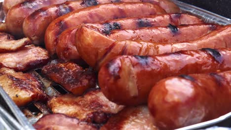 Closeup-view-of-bacon-and-meat-sausages-on-the-grill-with-smoke