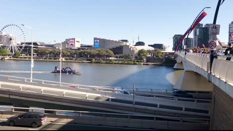 Barge-travels-up-Brisbane-river-towards-Grey-St-bridge-with-The-Wheel-of-Brisbane-and-South-Bank-in-distance
