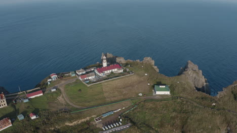 Slow-aerial-pivot-shot-around-Gamov-lighthouse-complex-standing-on-a-rocky-steep-cliff,-on-the-sunset