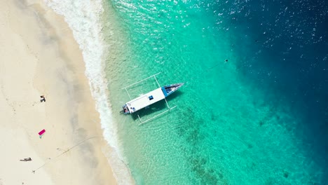 Traditionelles-Balinesisches-Libellenboot-In-Der-Nähe-Des-Sandstrandes,-Das-Im-Türkisfarbenen-Meerwasser-Schwimmt