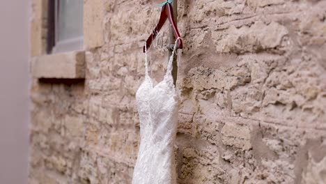 Wedding-dress-hanging-on-wooden-hanger-in-front-of-stone-wall-inside-beautiful-church