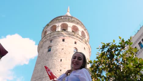 Attraktives-Junges-Schönes-Mädchen-Schwenkt-Türkische-Flagge-Vor-Dem-Galata-Turm,-Einem-Beliebten-Wahrzeichen-In-Istanbul,-Türkei