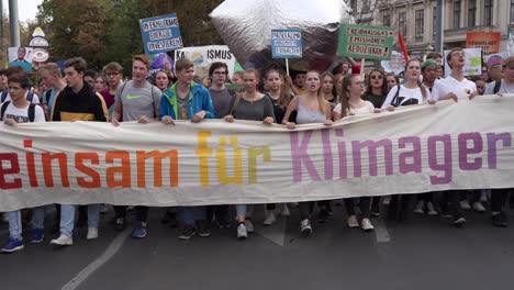 Frontal-following-view-of-kids-and-teenagers-walking-and-holding-banner-during-fridays-for-future-climate-change-protests