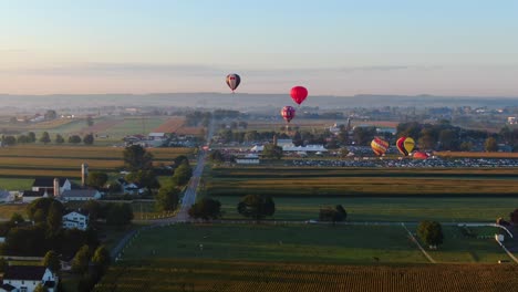 Drohne-Steigt-über-Maisfeld-Herab,-Während-Heißluftballons-Auf-Dem-Festival-Aufgeblasen-Werden-Und-über-Den-Morgenhimmel-Fliegen