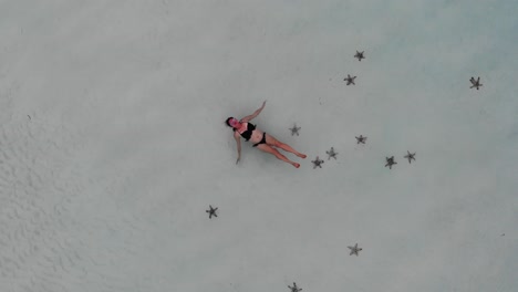 4K-aerial-rising-shot-of-young-lady-floating-on-her-back-near-the-beach-surrounded-by-starfish