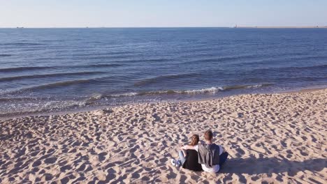 Aerial-Shot-Of-Young-Couple-Sitting-On-Sandy-Beach,-Hugging,-Holding-Hands