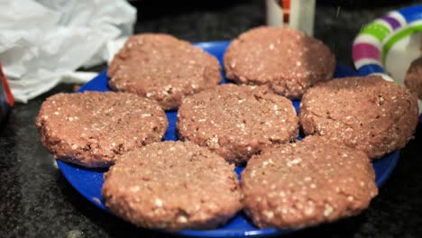 Seasoning-plant-based-burger-patties-on-a-blue-plate-for-a-summertime-barbecue-cookout,-in-slow-motion-4k