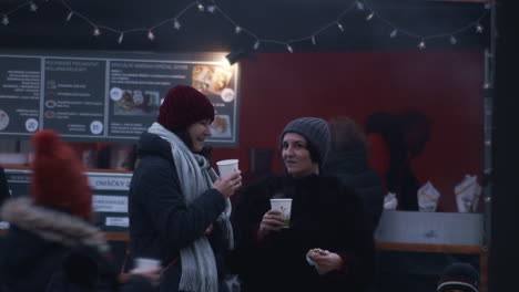 Two-women-chat-with-hot-drinks-in-outdoor-Christmas-Market-in-Prague
