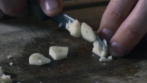 Close-up-of-a-mans-fingers-cutting-garlic-into-pieces-with-a-knife