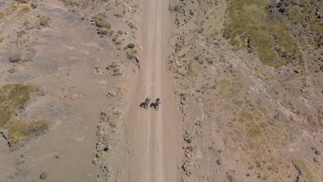 aerial-shot-following-two-mountain-bikers-climbing-up-a-gravel-road-mountain-pass