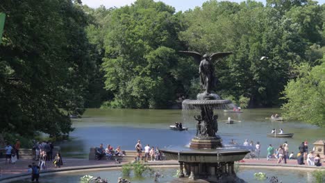 Slow-motion-establishing-shot-of-Bethesda-Fountain-and-The-Lake-behind-it-with-people-enjoying-a-sunny-summer-day-around-it-in-Central-Park,-New-York-City