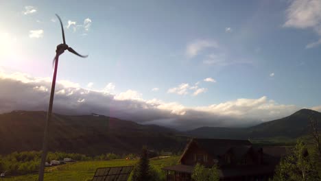 A-wind-turbine-is-seen-spinning-near-a-cabin-with-a-mountain-nearby