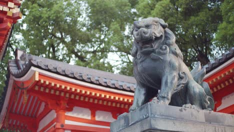 Stone-lion-statue-surrounded-by-a-shrine-and-tall-trees-in-the-background-in-Kyoto,-Japan-soft-lighting-slow-motion-4K